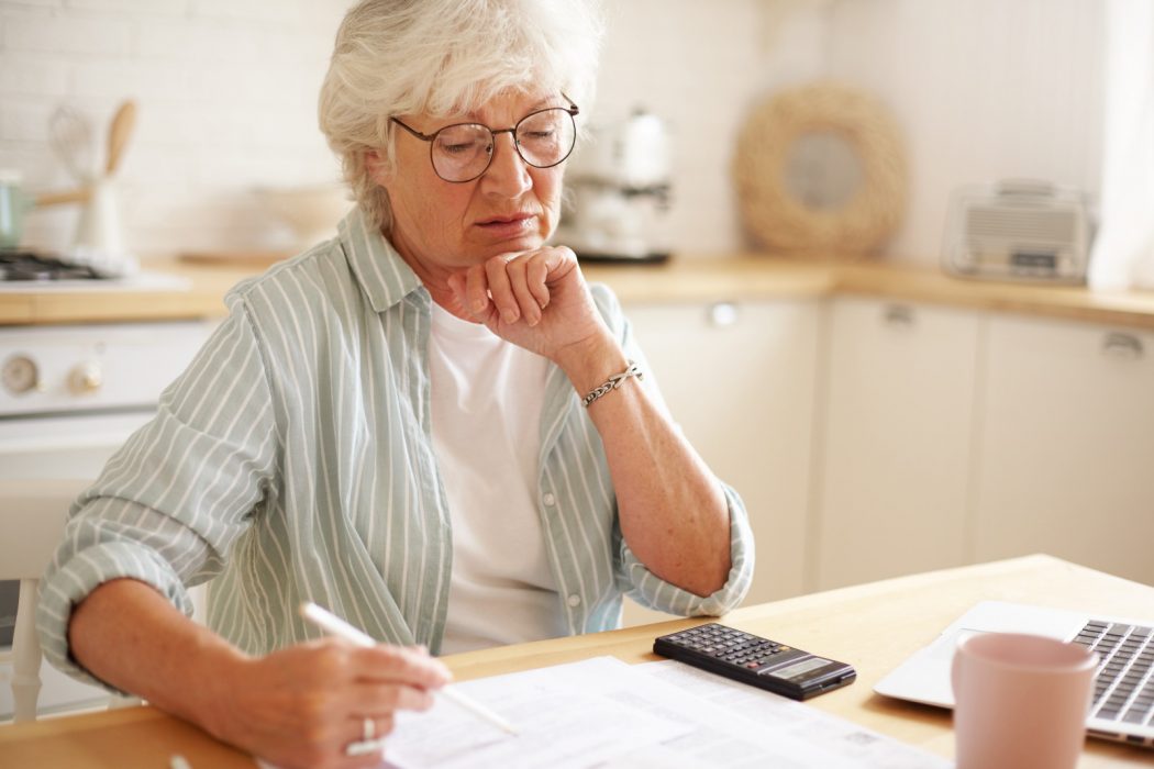 candid-shot-of-serious-caucasian-retired-woman-in-spectacles-calculating-expenses-trying-to-save-money-for-expensive-purchase-paying-domestic-bills-online-using-electronic-gadget-at-kitchen-table